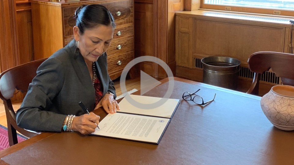 Secretary Haaland sits at a table and signs papers