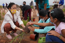 Secretary Haaland works with two youth to do conservation work by planting plants. Others work in the background. 