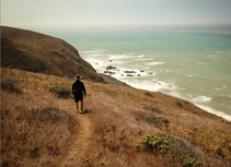 A man standing on a path looking at the pacific ocean.