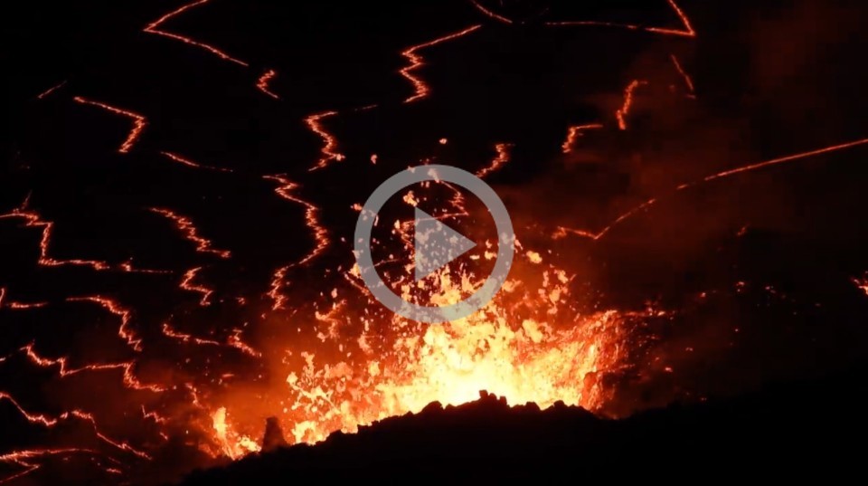 A volcano at night glows orange with hot lava