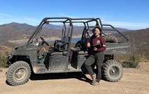 A woman standing next to a off-road vehicle above a lake.