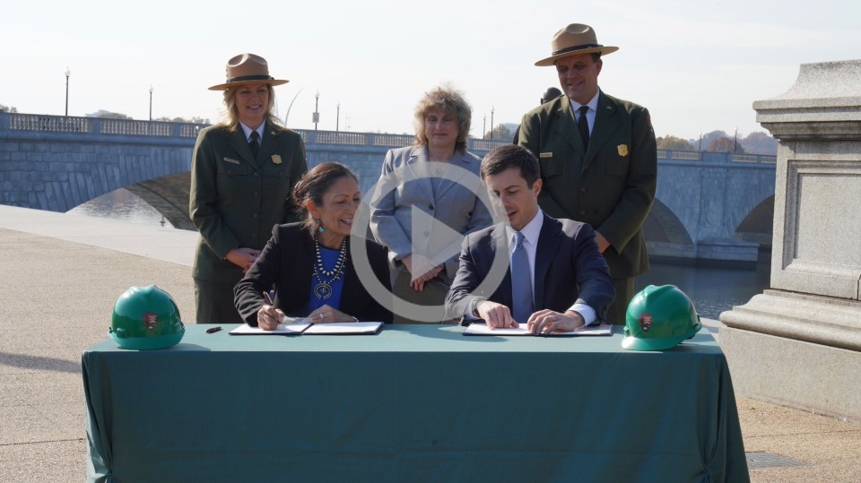 Two park rangers stand next to Secretary Haaland as she signs paperwork