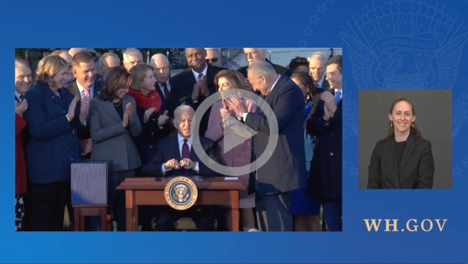 A group of people stand behind President Biden as he signs legislation