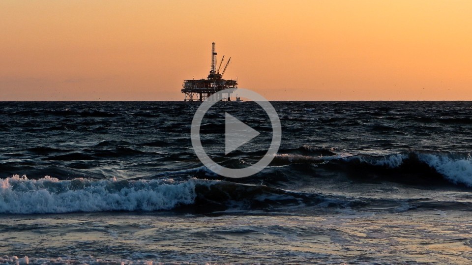 An oil and gas rig sits in the ocean off the coast. 