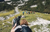 Hikers walking on a single-file trail up a mountain.