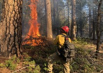 A firefighter standing next to a pile of burning wood.