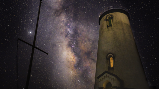 A lighthouse sits underneath a dark and starry night sky