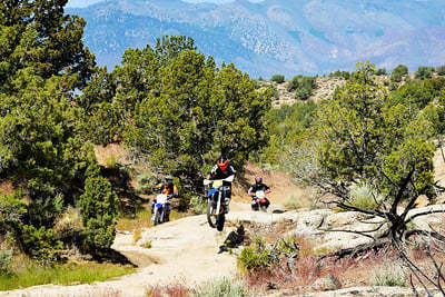 People on dirt bikes jumping a large rock.