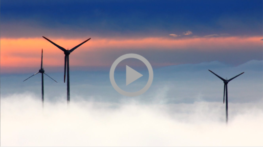 Ocean wind turbines poke above the clouds and fog at sunset