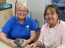 Two women sitting at a table that has many arrowheads on it.