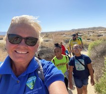 BLM employee Tracy Albrecht smiles in a selfie with several youth behind her on a trail in a desert landscape. 