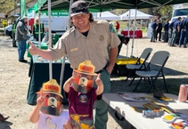 A uniformed man and two kids giving a thumbs up, while the kids are wearing Smokey the Bear masks.