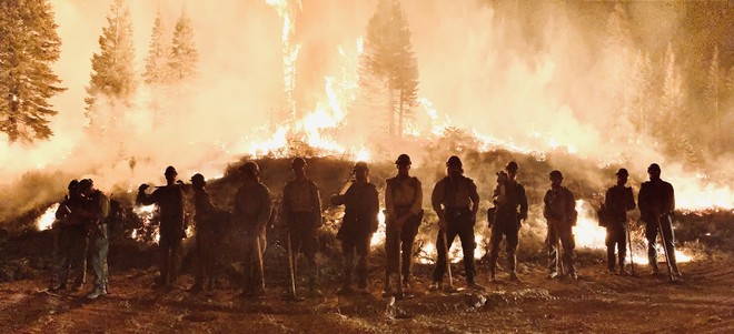 Firefighters standing in a line for a photo in front of fire.