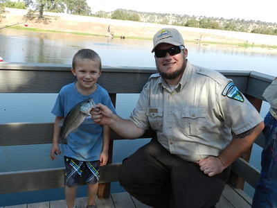 A park ranger holds a fish for a boy.