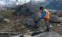 A person standing on a large rock on top of a mountain with a clipboard in their hand.
