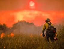 A firefighter in a file with fire burning in the distance. 