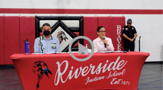 Secretary Haaland and Assistant Secretary Newland seated at table inside Riverside Indian School gym