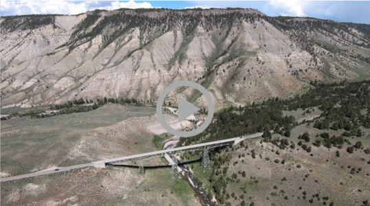 Aerial view of mountains at Yellowstone National Park; a bridge carrying traffic crosses over a tall bridge below 