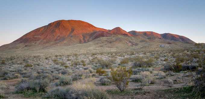 A mountain lit up red by the sunset in a desert.