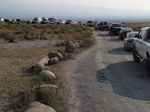 A dirt road lined with cars that are parked in a desert area.