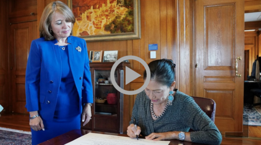 Secretary Deb Haaland signs a document as Assistant Secretary Carmen G. Cantor look on