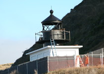A lighthouse under renovations with a fence around it.