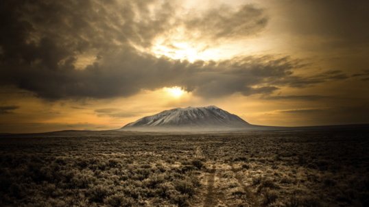 The sun lights a large butte during a dramatic sunset and is surrounded by open plains.