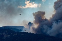 Smoke plume from a wildfire with two aircraft in the sky.