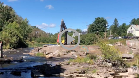Large machinery knocks down a concrete dam on a river