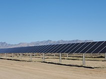 Solar panels with dirt in the foreground and mountains in the background. 