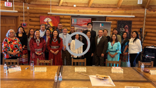 Secretary Haaland poses with students, faculty and others in a log-paneled room at Southwestern Indian Polytechnic Institute.