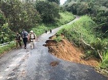 Three men walk next to a mud damaged road.