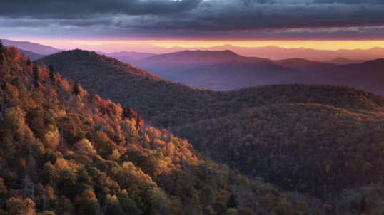 Fall colors dot the mountain side as the sky turns pink and purple at sunset