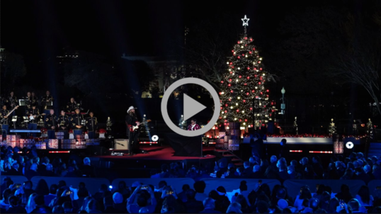 The National Christmas Tree surrounded by performers and musicians on a stage, the White House in the background