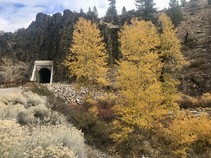 View of tunnel entrance with dirt trail leading to it, fall foliage on trees on either side.