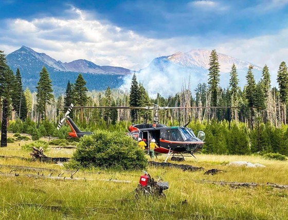 Members of a Yosemite helitack crew work around a helicopter in a grassy field with smoke rising in the distance. Photo by Yosemite National Park.