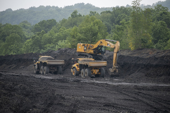 Two dump trucks and an excavator reclaim an abandoned mine land.