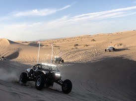 An off-highway vehicle sits in the foreground of a desert landscape's expansive dunes.