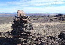 A cairn, or stacked rocks, sit in foreground of a high desert landscape of hills and mountains. 