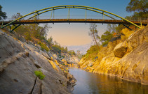 A large bridge spans over the San Joaquin River's gorge. The sides of the river lined with impressive granite rock formations.