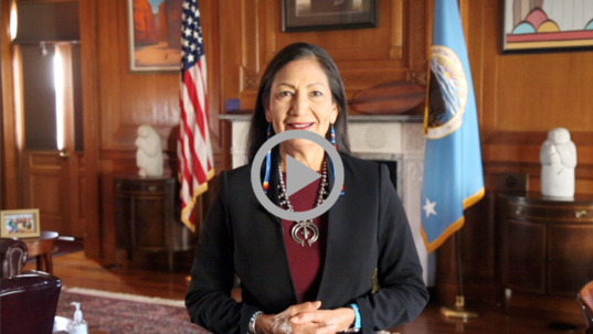 A photo of Secretary Deb Haaland in front of a fireplace 
