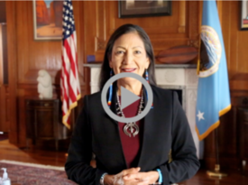 A closeup of Secretary of Interior Deb Haaland with a video "play" icon graphic overlay. 