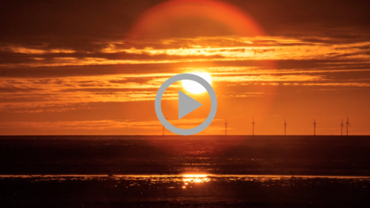 Sunset over the ocean behind a row of wind turbines