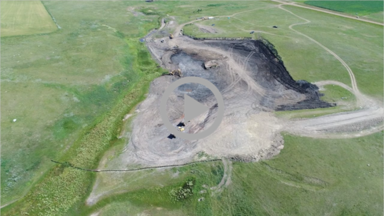 Aerial view of a coal mine and mine equipment surrounded by grassy hills 