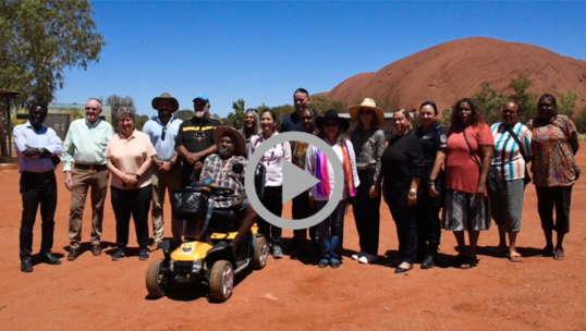 Secretary Haaland, Ambassador Kennedy, and Assistant Secretary Newland standing in front of Uluru with members of the Mutitjulu community.