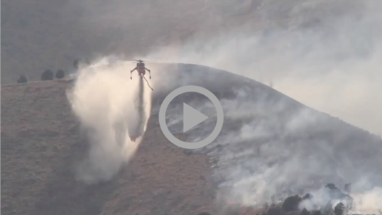 A firefighting helicopter dumps chemicals on the scene of a wildfire