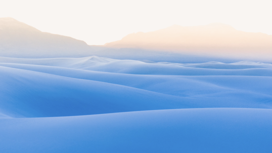 A vast landscape of white sand dunes is overseen by a distant, hazy mountain.