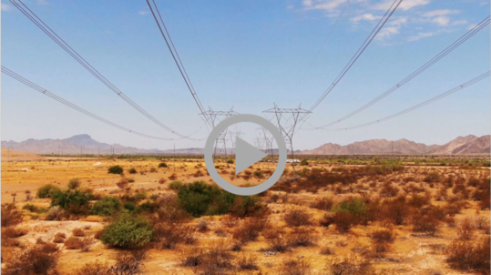A power transmission line stretches into the distance above a desert landscape.