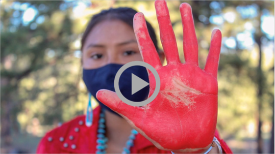 A Native woman holds up her red-painted hand. 