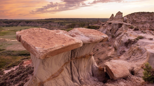 A sun sets over an unspoiled badlands landscape with dry terrain, rocks and reddish-brown colored soil.